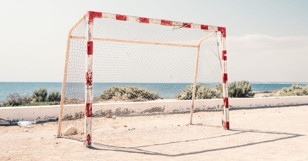 Red and white goal posts with net on a beach in front of ocean